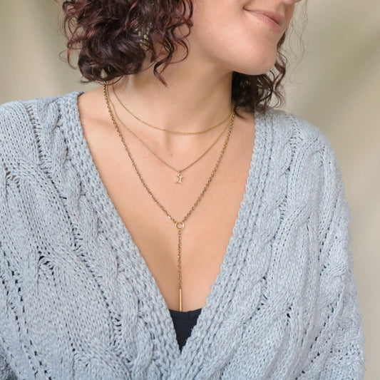 Woman wearing a light blue knitted cardigan with a zodiac layered gold necklace on.
