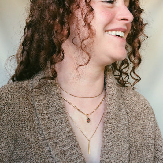 Woman with curly hair wearing a beige cardigan and layered necklaces against a plain background