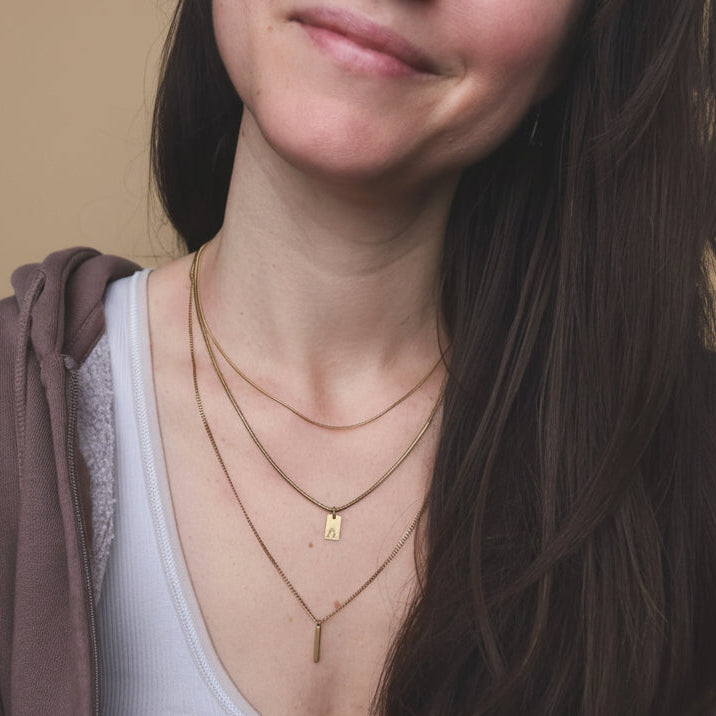 Close-up of a person wearing multiple gold necklaces with a neutral background
