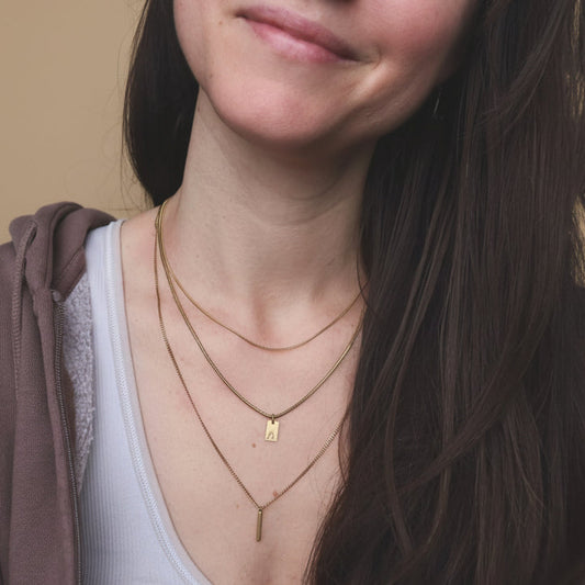 Close-up of a person wearing multiple gold necklaces with a neutral background