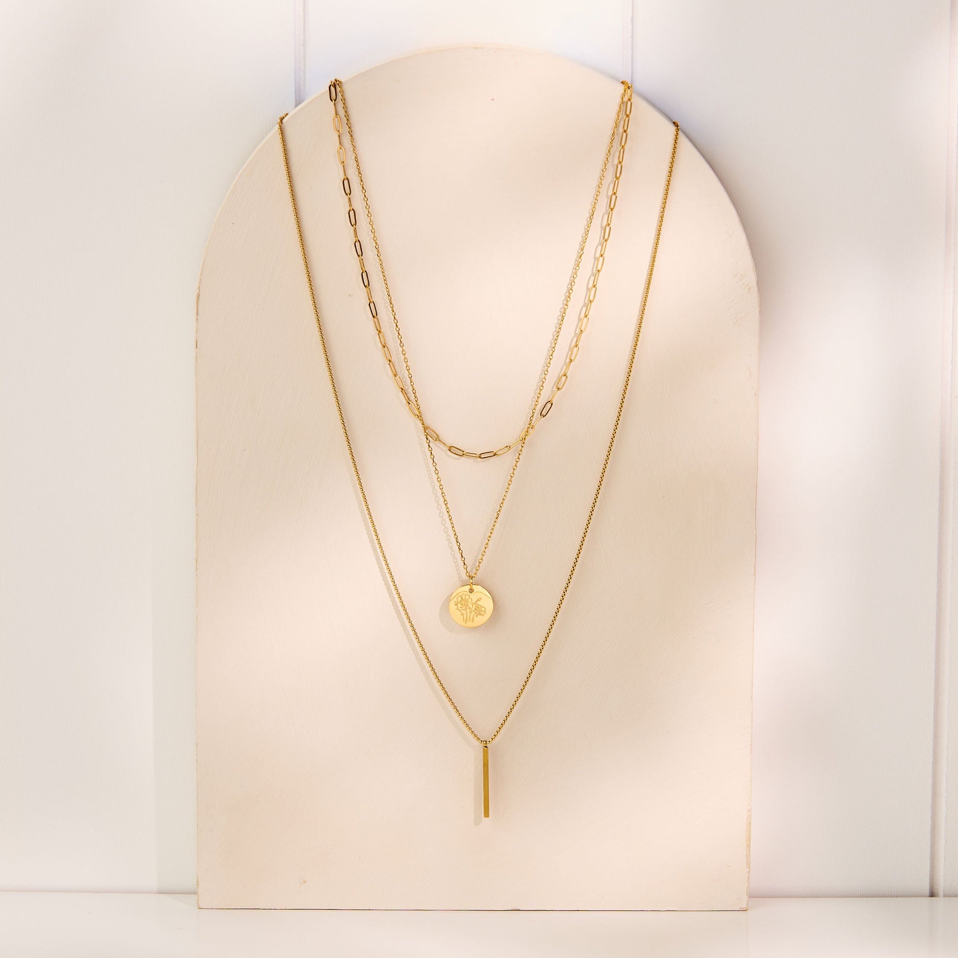 Three gold necklaces displayed on a white stand against a white background