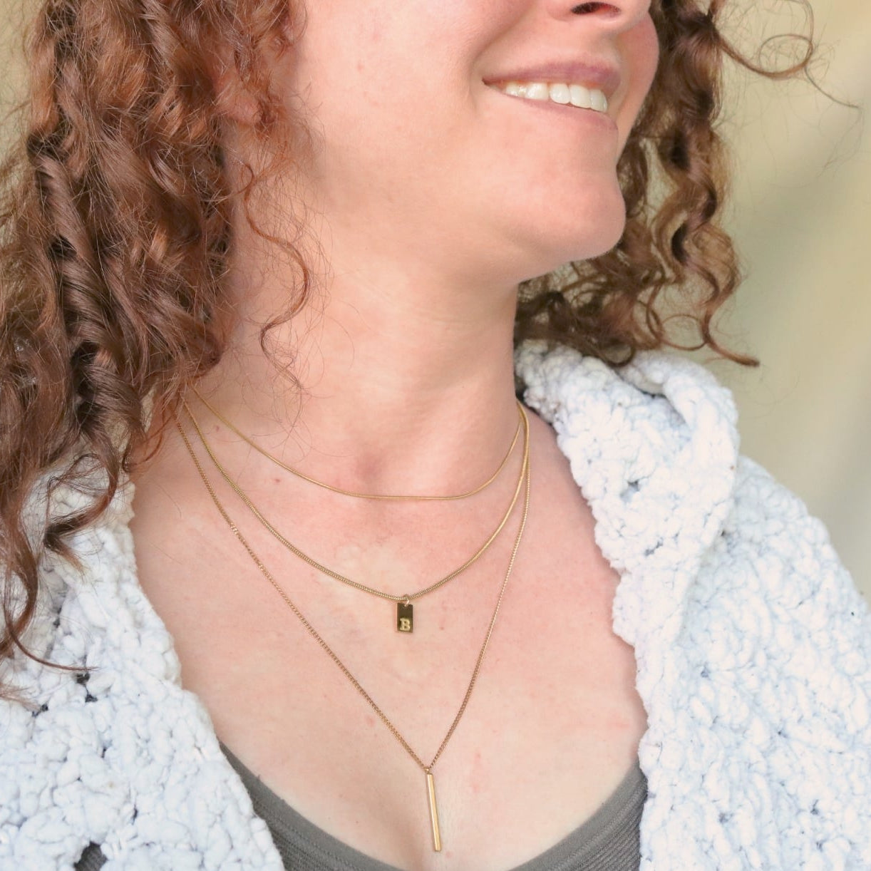 Woman wearing a light blue cardigan and layered necklaces with a neutral background