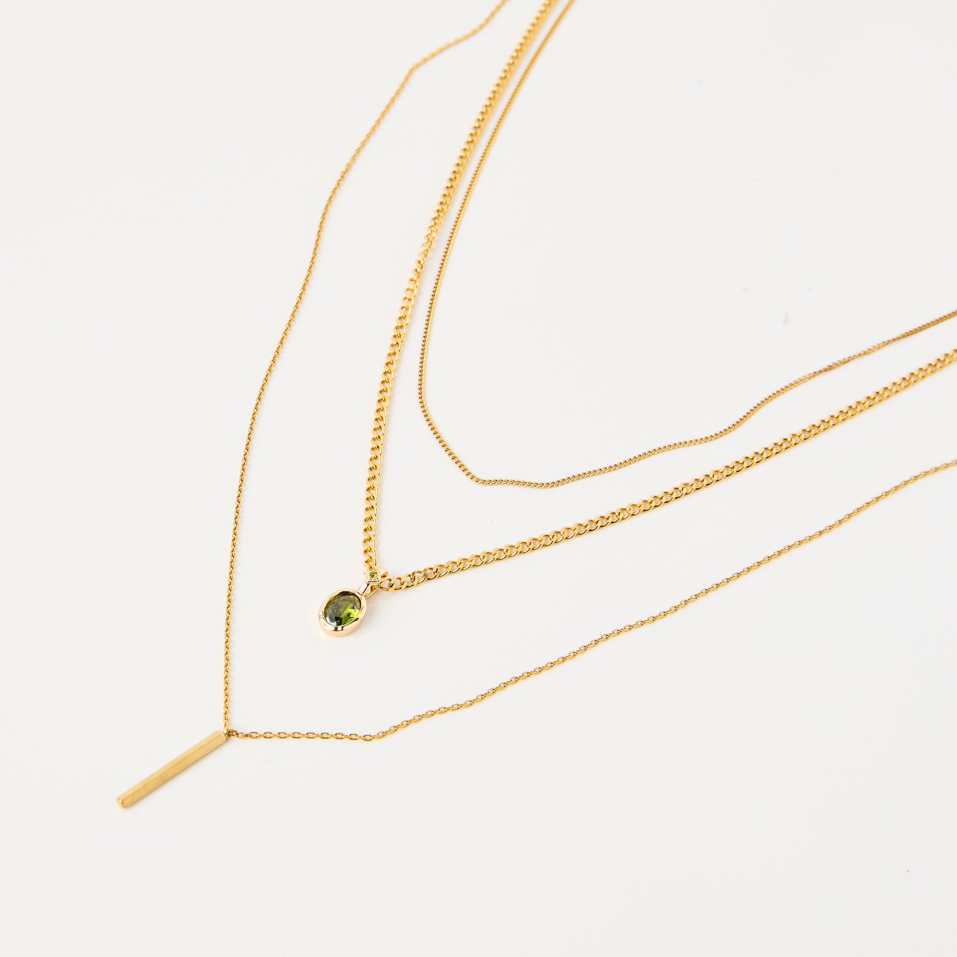 Three gold necklaces with a green gemstone on a light gray background