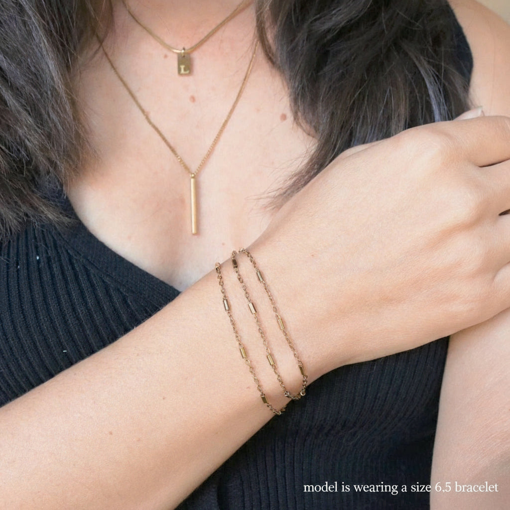 Person wearing gold jewelry including necklaces, bracelets, and a ring.