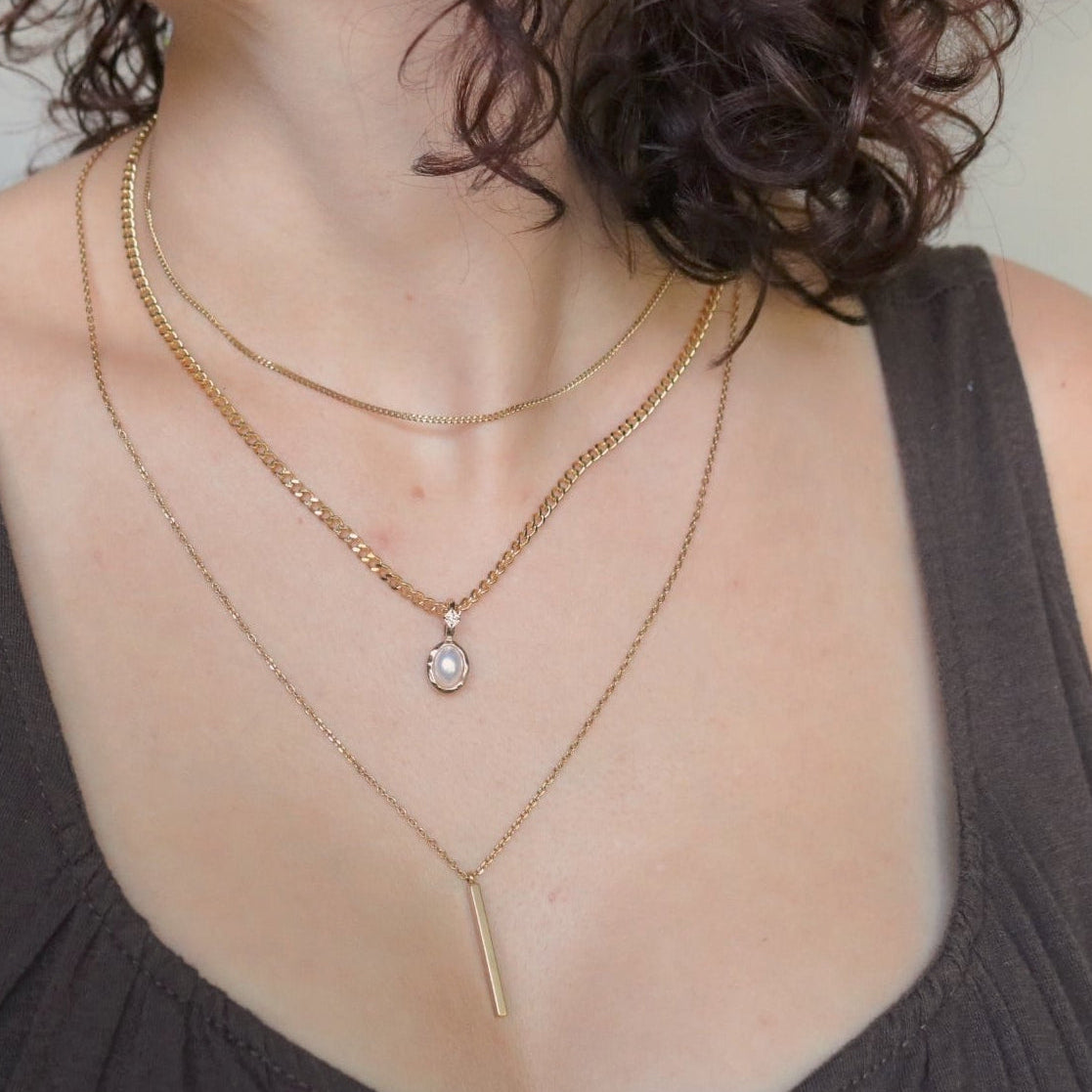 Person wearing multiple gold necklaces with a June Pearl Birhstone charm.