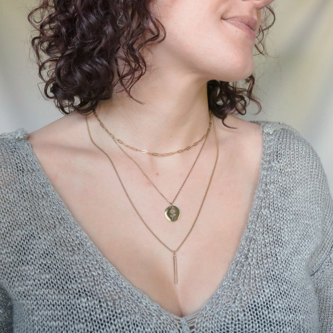 Woman wearing a gray sweater with a deep neckline and layered necklaces against a neutral background