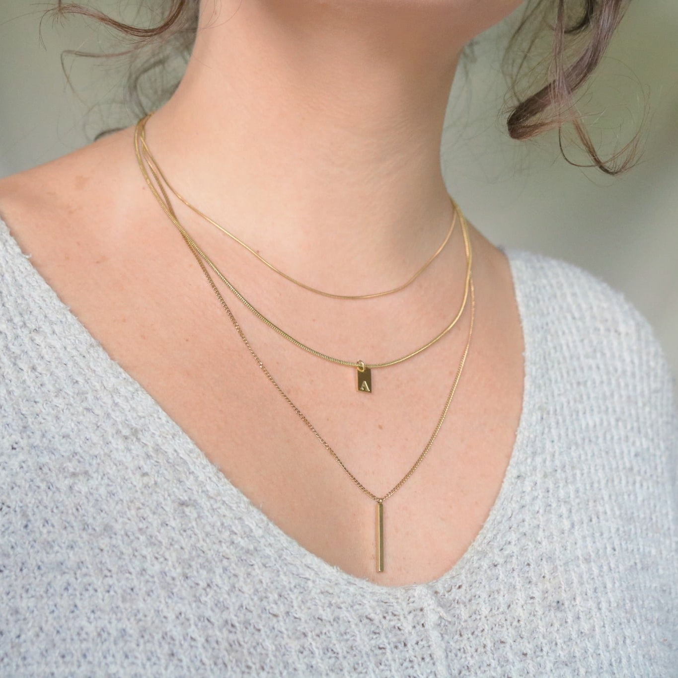 Close-up of a person wearing multiple gold necklaces on a light gray background