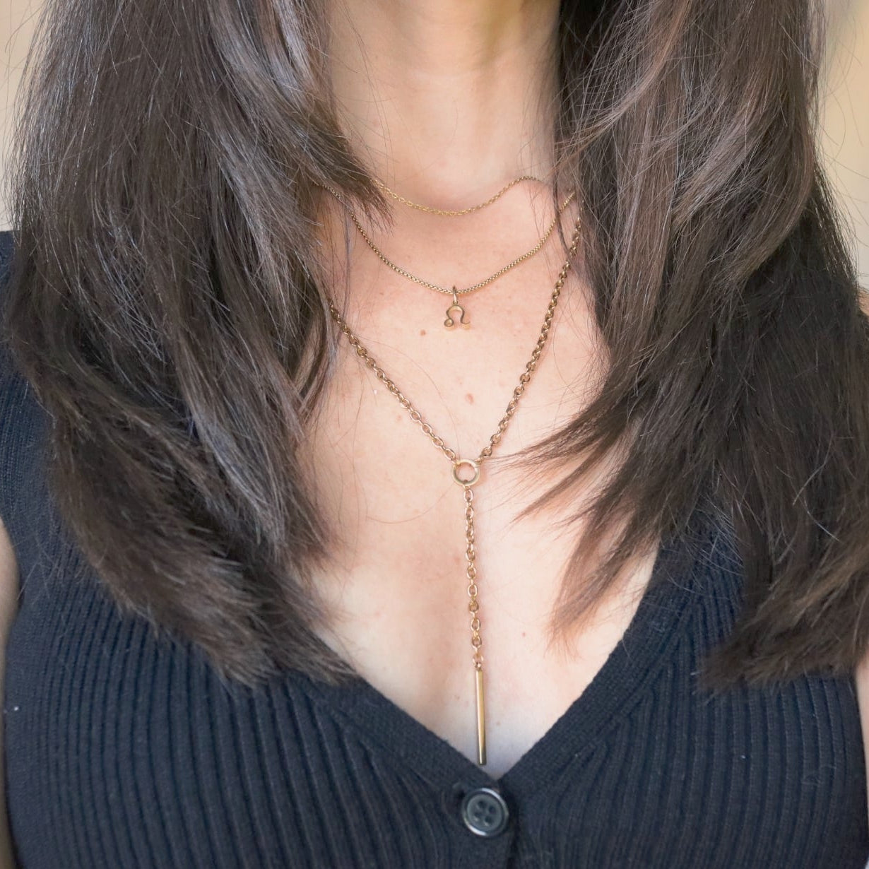Person wearing a black sleeveless top with layered necklaces.