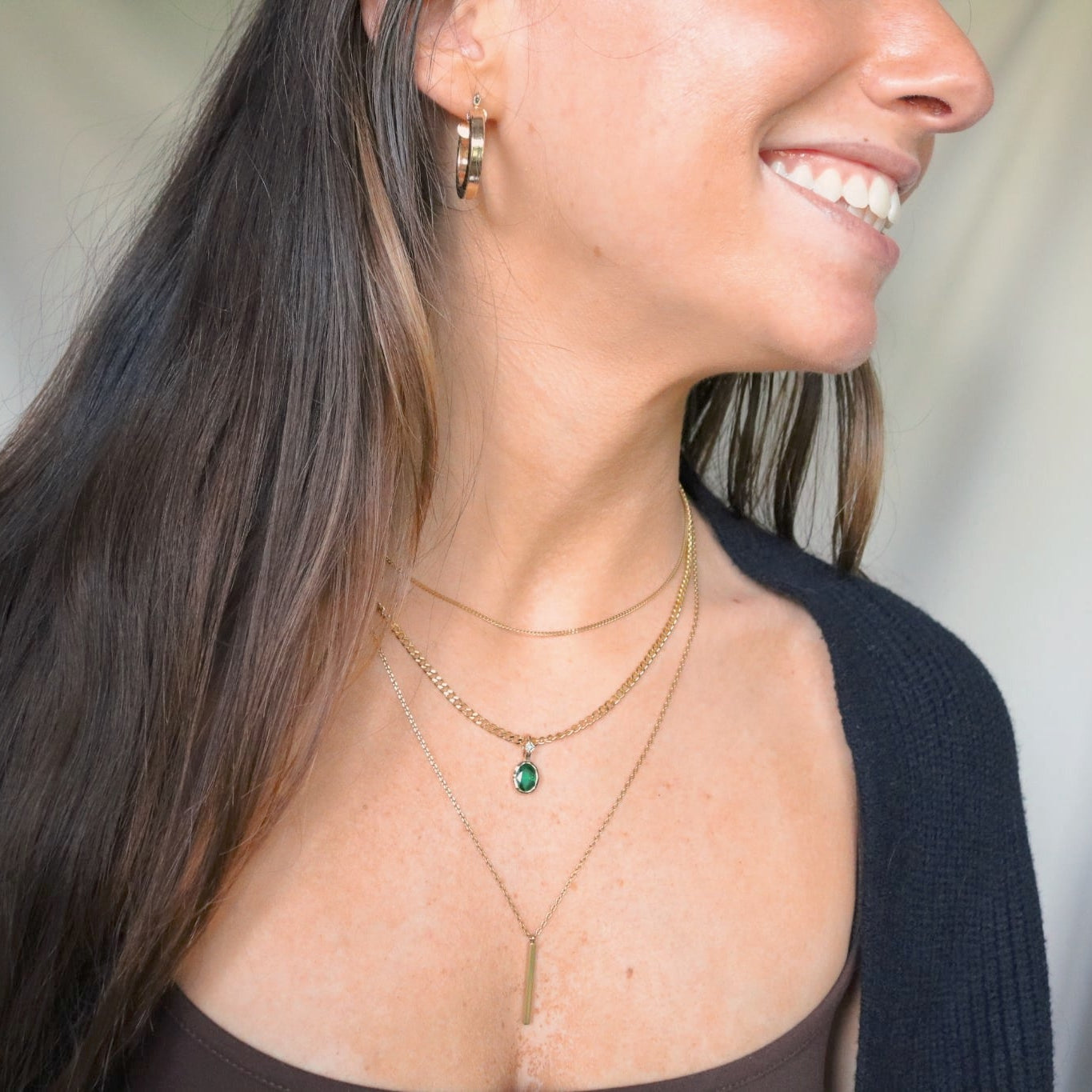 Woman wearing multiple necklaces with green May Birthstone charm.