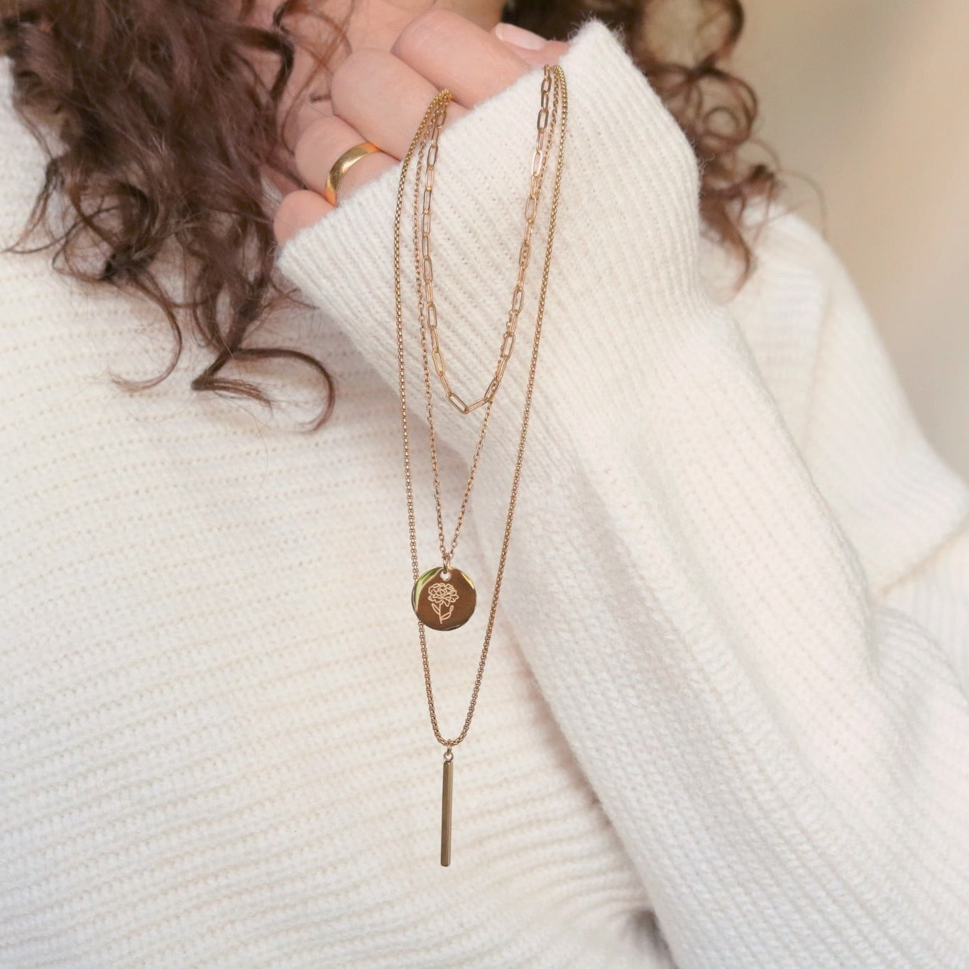 Person wearing a white sweater with layered gold necklaces