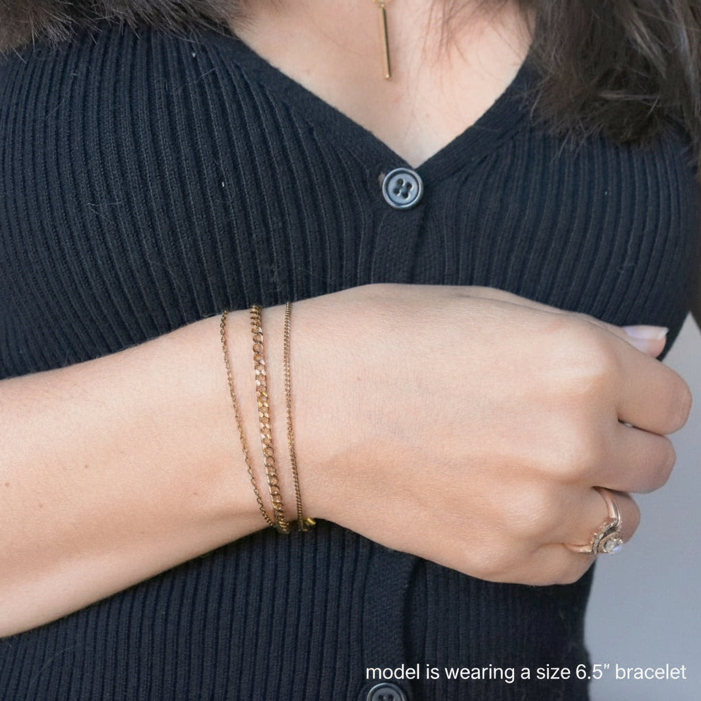 Person wearing a black sleeveless top with buttons, gold bracelet, and ring on a blurred background