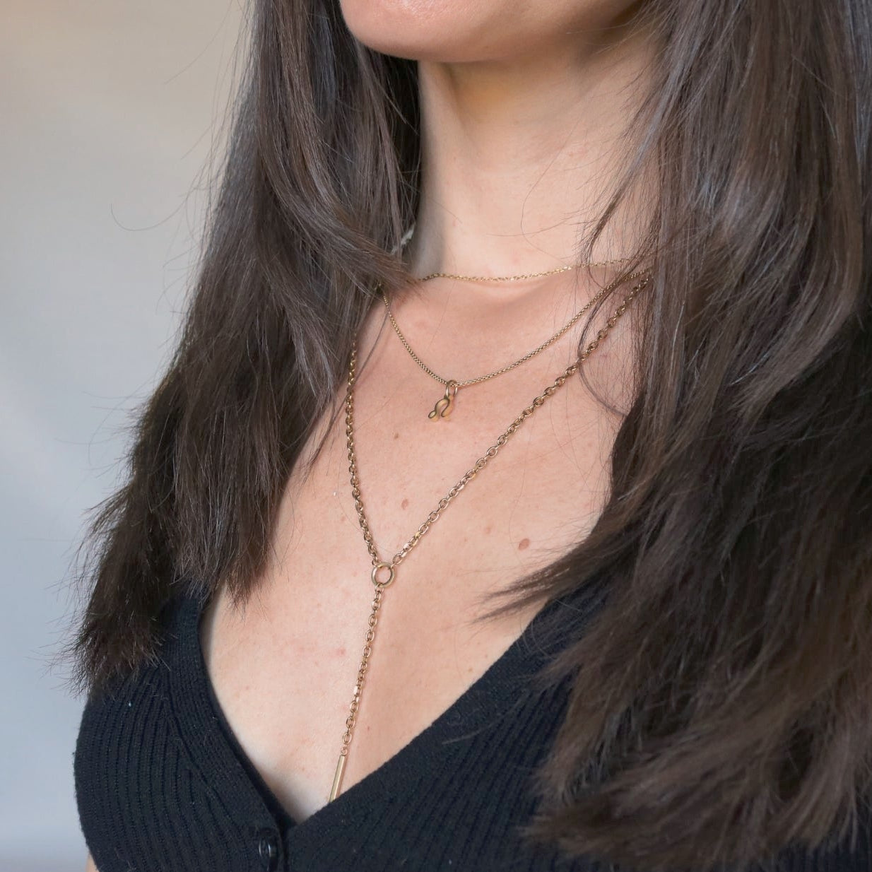 Woman wearing a black top and layered necklaces with a neutral background